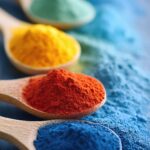Colorful display of artificial food dyes organized in wooden spoons on a blue background